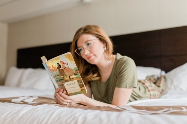 Woman reads Anne of Green Gables novel while lying on guest bed