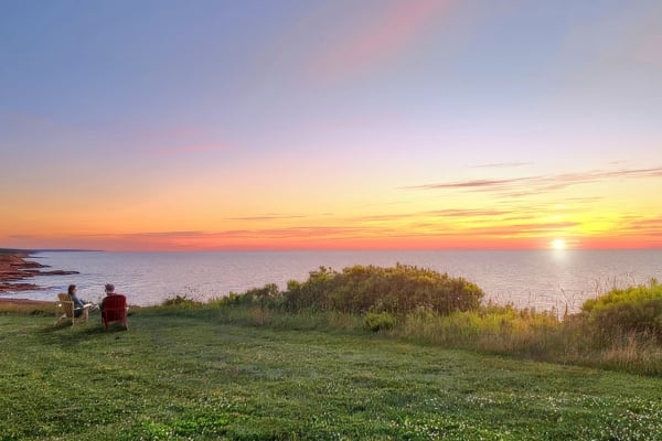 two people sit in lawn chairs with a PEI coastal view while watching a beautiful sunset