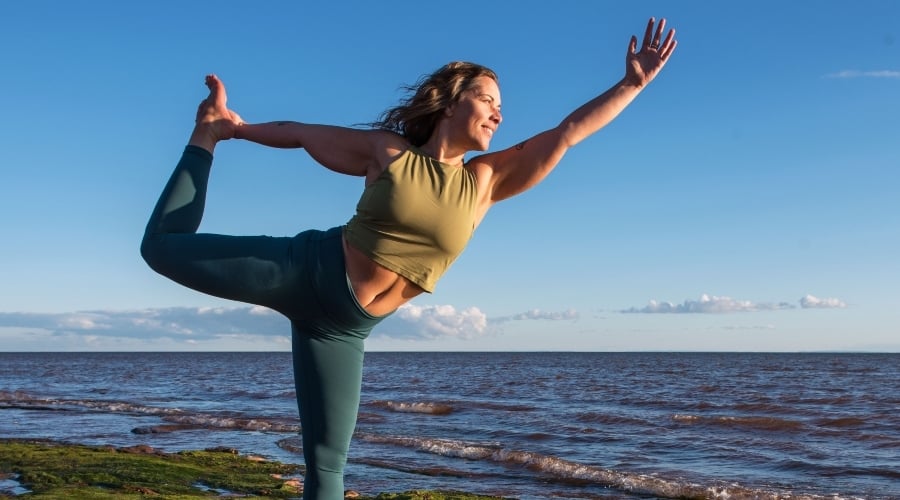 Woman does yoga pose at Canoe Cove beach under a blue sky, PEI