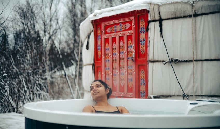 Woman in outdoor hot tub with yurt in background in winter