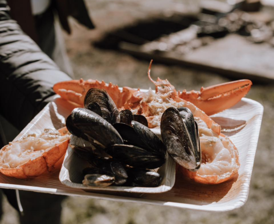 Plat of freshly cooked halfed lobster and steamed PEI Mussels in outdoor setting