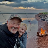 Wade and Marney MacKinnon with fishing rods in hand and a campfire on the beach