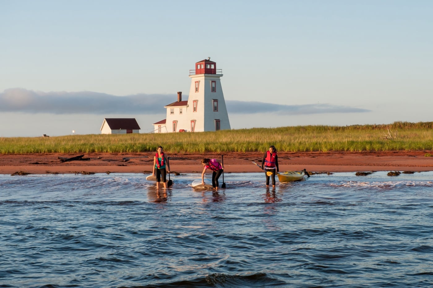 Three persons on paddleboards and kayak near lighthouse
