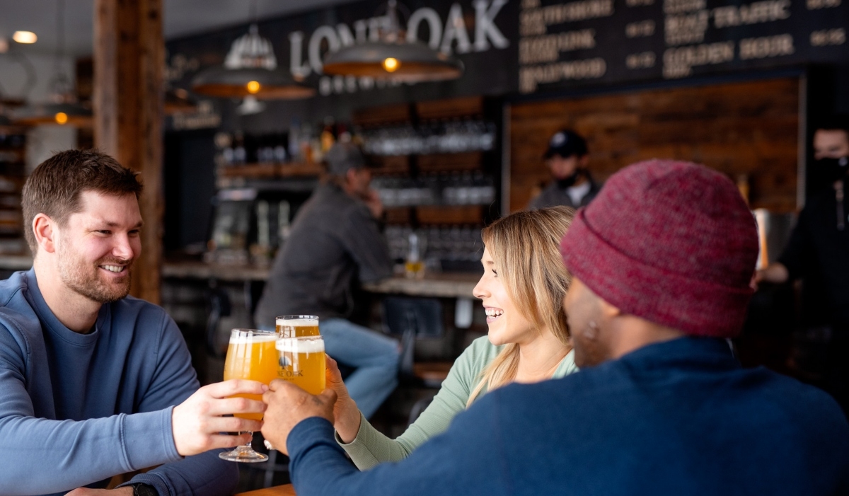 THree people raise a glass of beer at Lone Oak Brewing Co