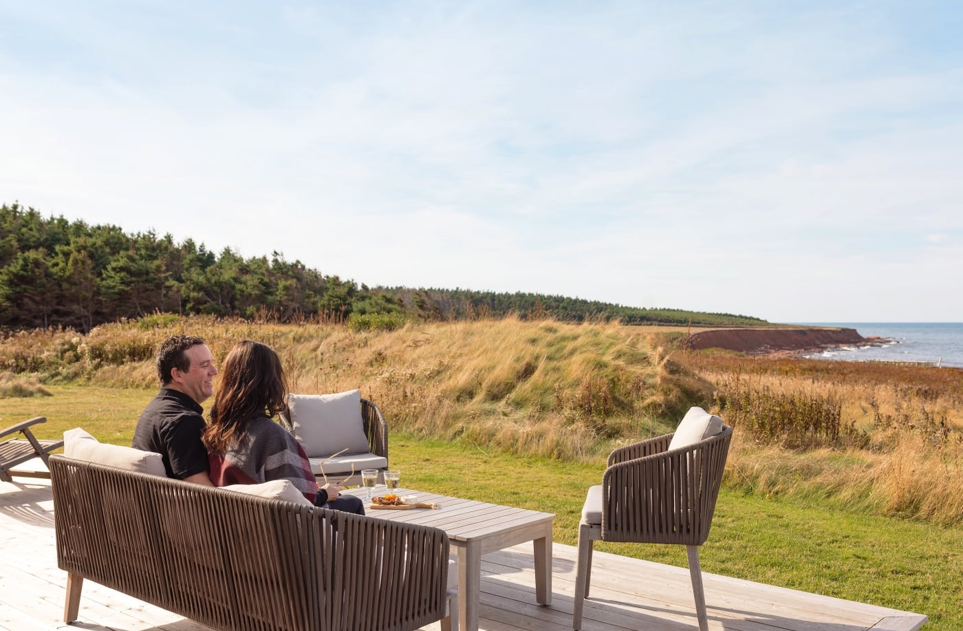 Couple sit on deck overlooking coastal view of red cliffs and water
