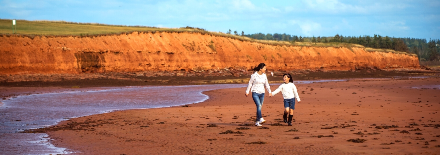 Argyle Shore, PEI Adult and child walk along the sand with red cliffs in background at Argyle Shore Provincial Park