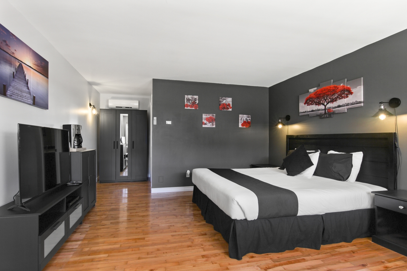 Large bedroom wit hardwood floors, grey and white accent walls highlighted by red accent decor