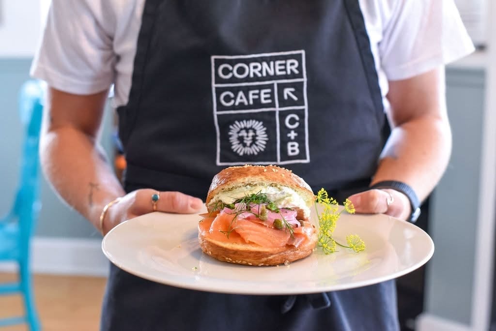 Plated smoked salmon bagel with server wearing C&B Corner Cafe apron