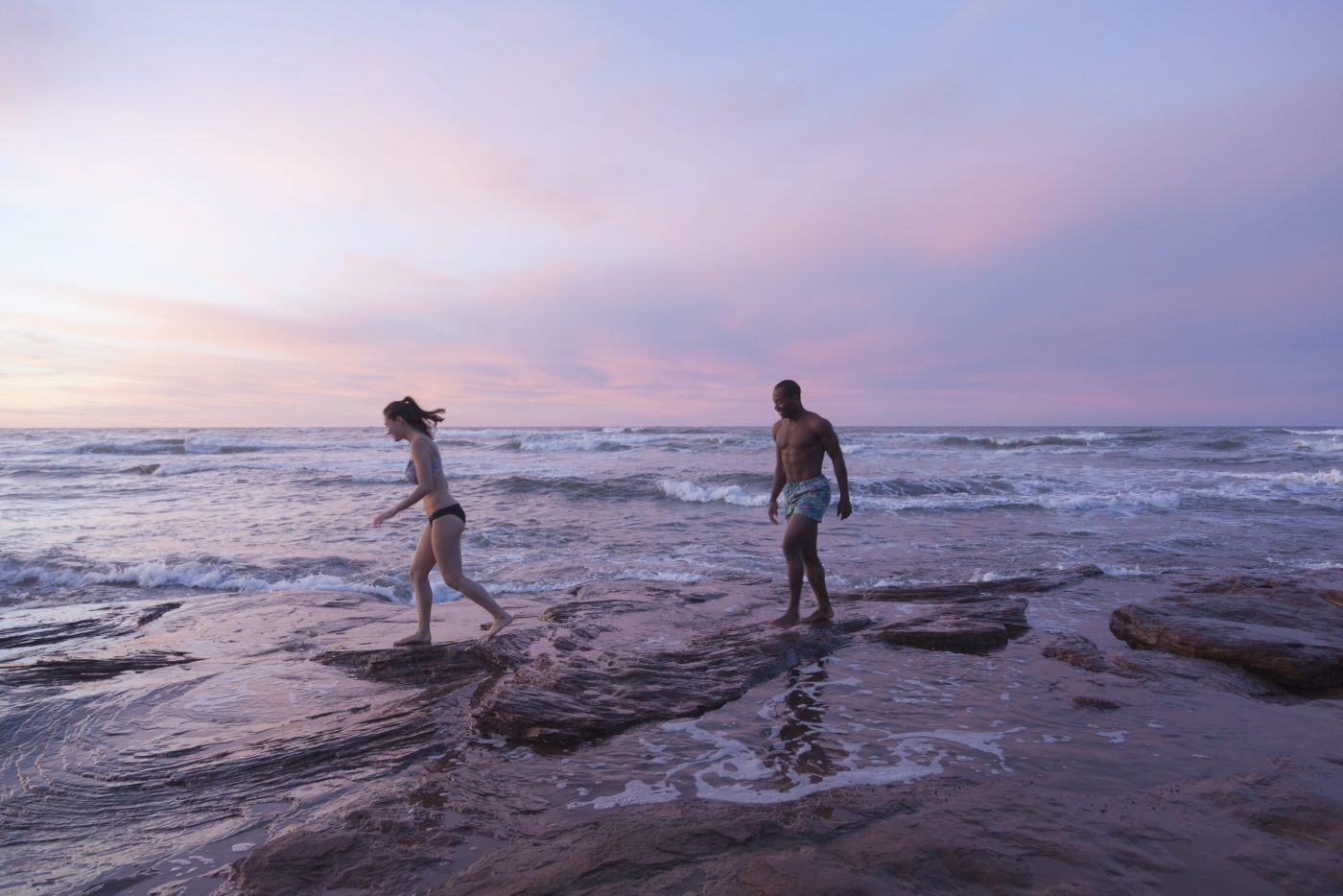 Couple walk on rocks at Cavendish Beach at sunset