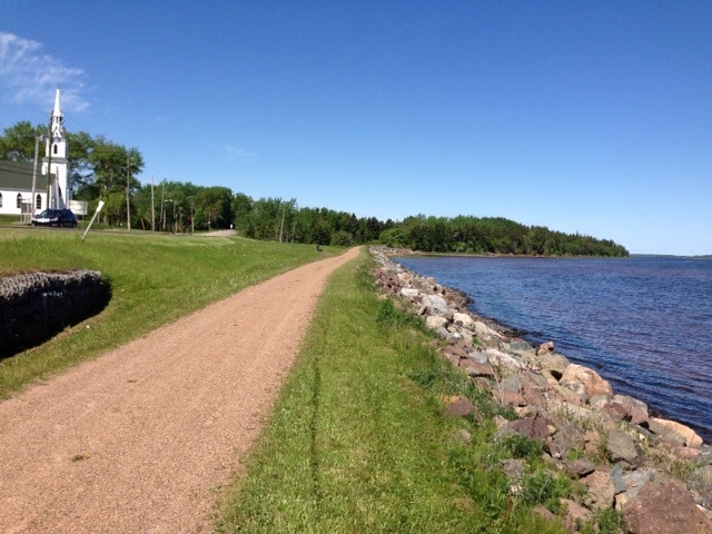 Confederation Trail along St. Peters Bay PEI in summer with white church on one side and bay on the other