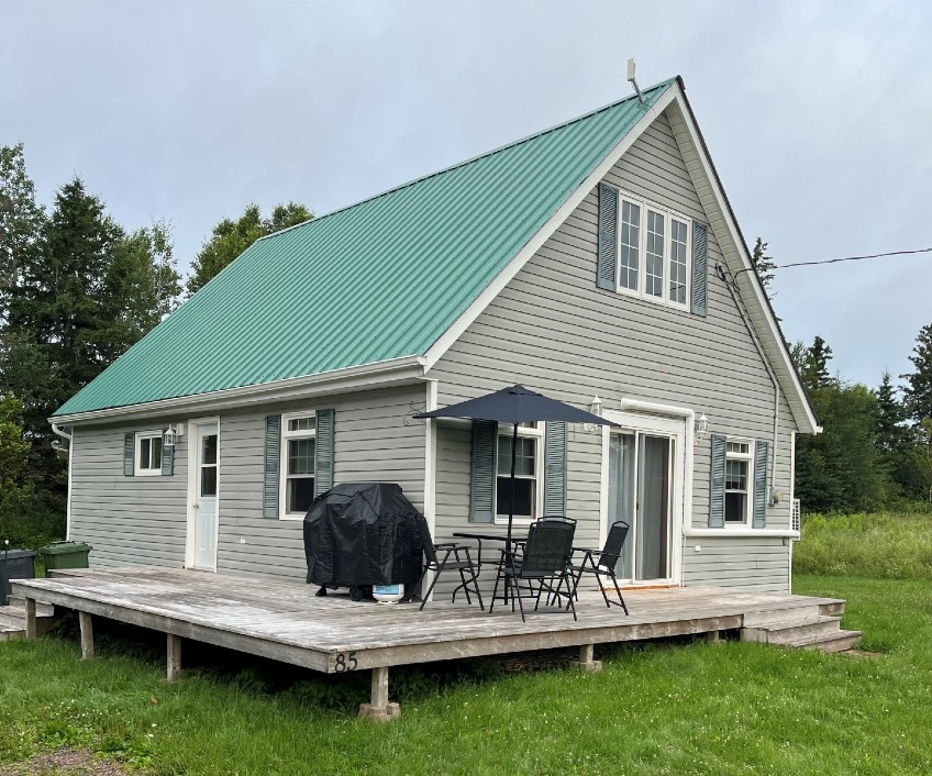 Outdoor image of Fogwell Cottage, light green siding with brighter green steel roof, wrap around deck