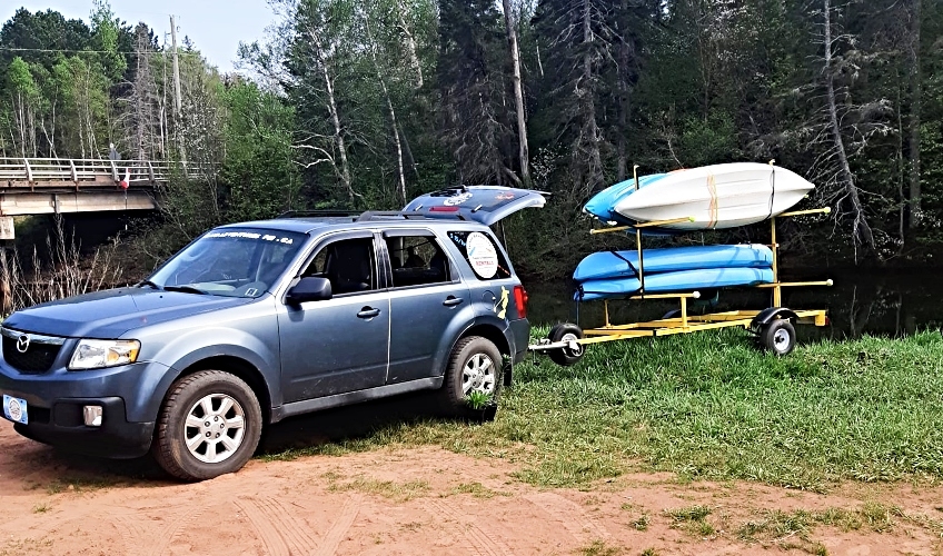View of truck and trailer with multiple kayaks parked next to a river