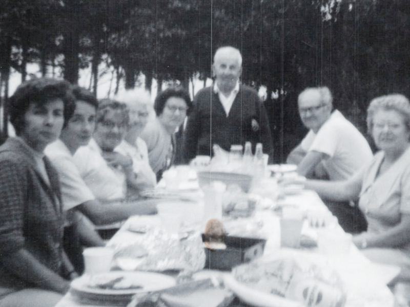 Vintage photo of eight adults sitting at a picnic table for dinner