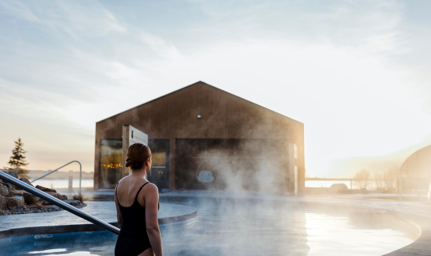 Person stands in hot tub looking over St. Peter's Bay in winter