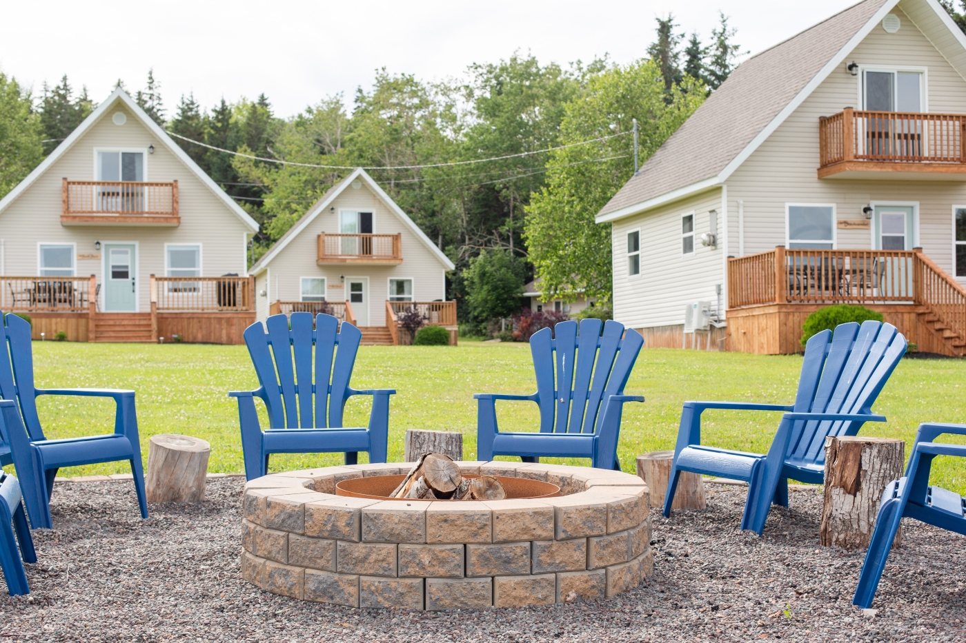 Blue adirondack chairs situated around a firepit in front of Oceanview Chalets