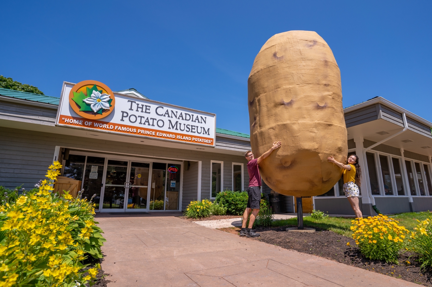 Two people stand with arms around big potato in front of the Canadian Potato Museum 