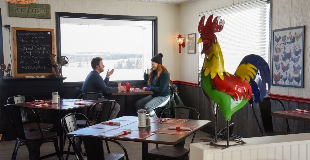 Rooster decoration in foreground with couple sitting at table in background in front of window with winter scene