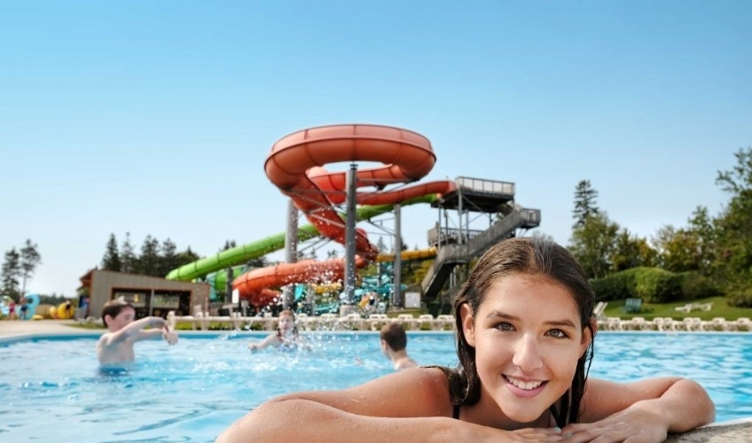 Young girl smiles on edge of pool with waterslides in background