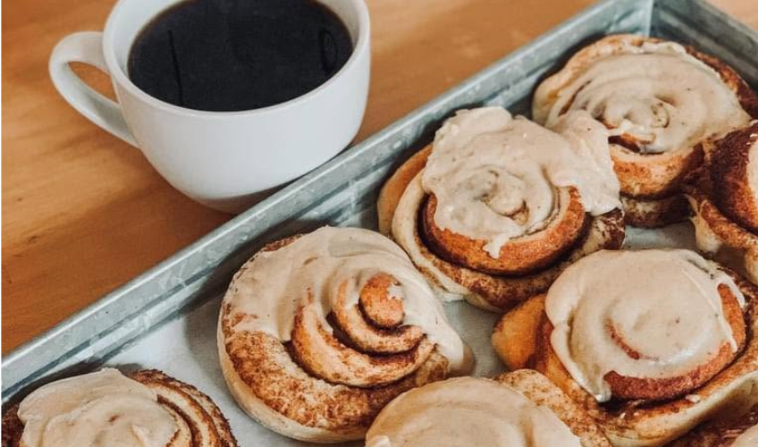 Tray of iced cinnamon rolls with cup of coffee to the side