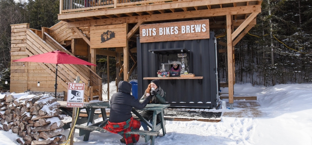 Couple sit at picnic table at Bits Bikes Brews in winter at Brookvale Nordic Park