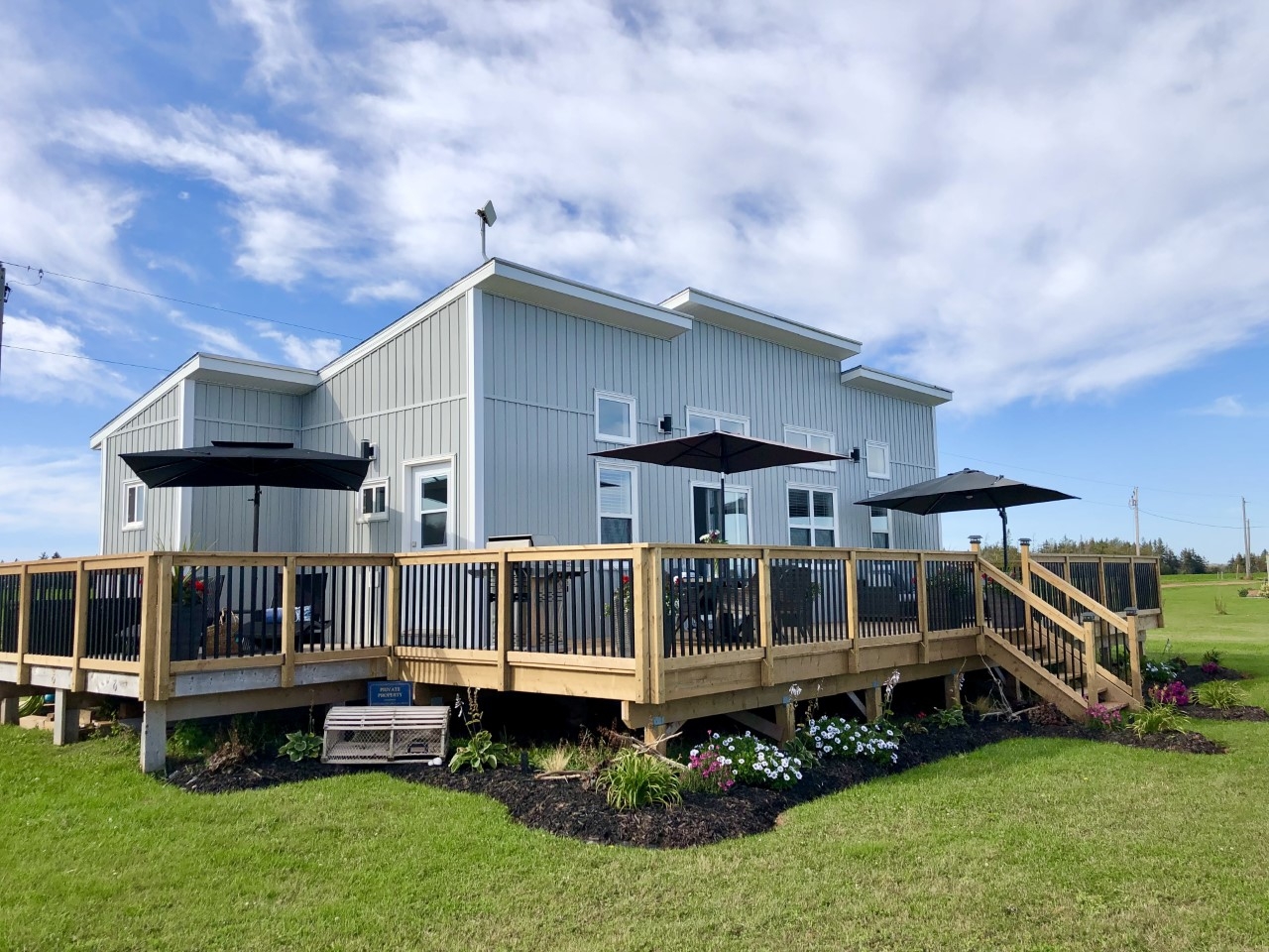 opulence on the Ocean large grey cottage surrounded by a deck with umbrella seating areas.