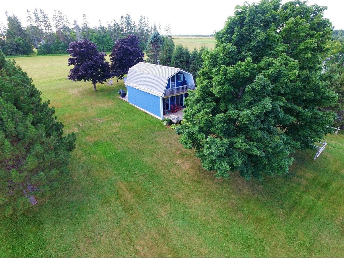 Quiet river view Airele view of blue hip roofed cottage flanked by trees.