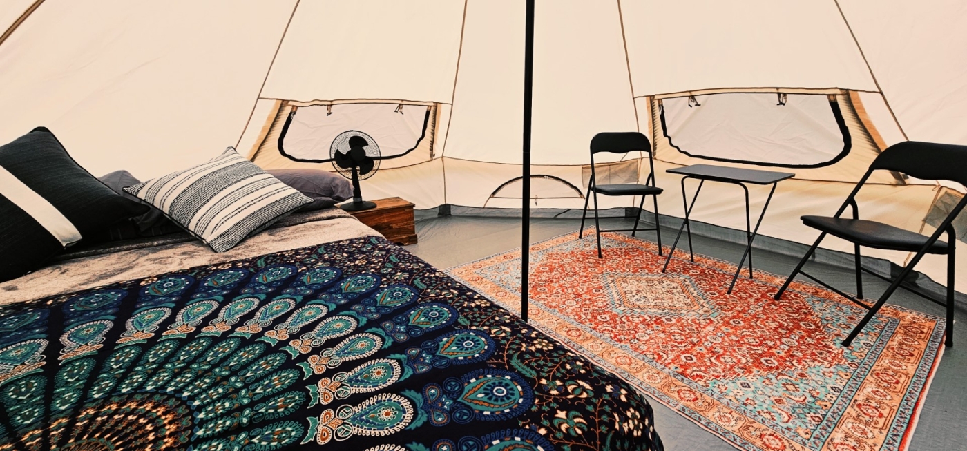 inside view of can host tent on property of the Red Fox Campground. Small Bistro set and bed with colorful bedspread.