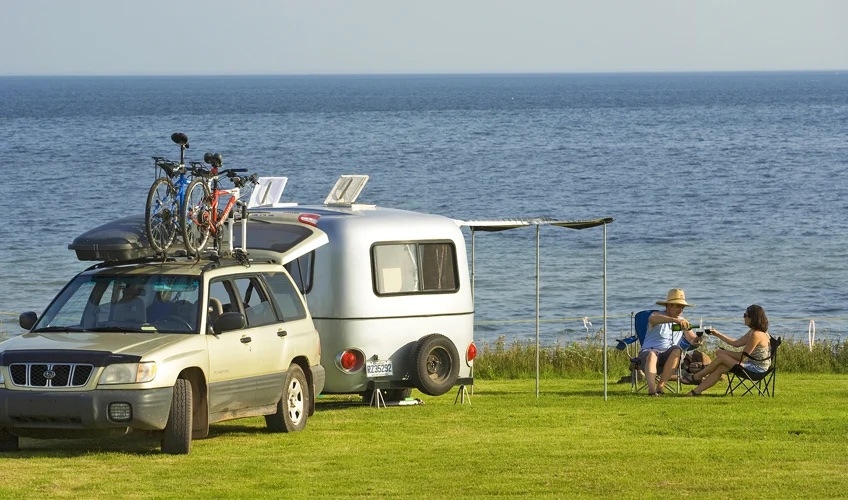 A couple camping next to the water with their car and RV parked beside them